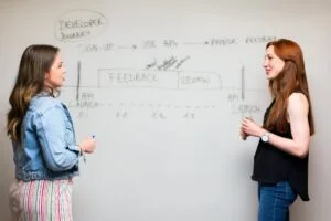 photo of women talking beside whiteboard